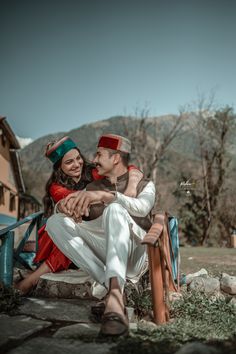 a man and woman sitting next to each other on a bench in front of mountains