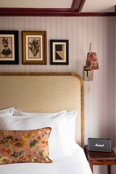 a bed with white sheets and pillows in a bedroom next to pictures on the wall