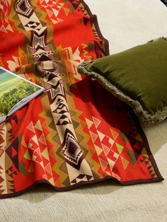 the blanket is laying on the floor next to an open book and a green pillow