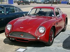 an old red sports car parked next to another one in a parking lot with other cars behind it