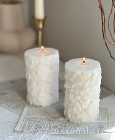 two white candles sitting on top of a newspaper