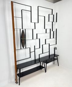 two benches are in front of a white wall with black lines on it and a long wooden pole