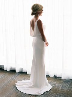 a woman standing in front of a window wearing a white dress and holding her back to the camera