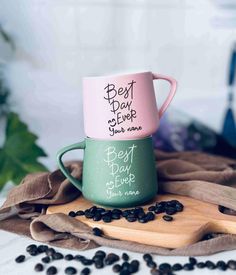 two coffee mugs sitting on top of a wooden cutting board next to black beans