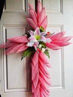 a cross made out of pink and white flowers on a front door with green leaves