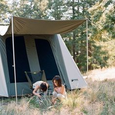 two children are playing in the grass near a tent that is set up in the woods