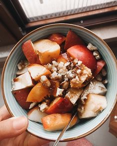 a bowl filled with fruit and nuts on top of a table next to a window