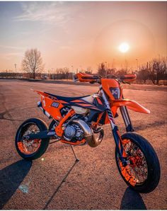 an orange and black dirt bike parked on top of a parking lot with the sun in the background