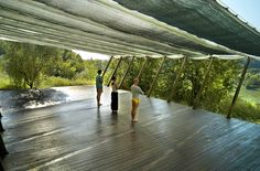 two people standing under an awning on a wooden deck with trees in the background