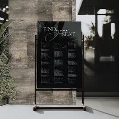 a black and white sign sitting in front of a wall with plants on it's sides