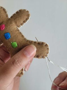 a hand holding a piece of brown felt with colored hearts on it and thread in the middle