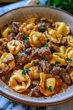 a bowl full of pasta with meat and sauce in it on a marble counter top