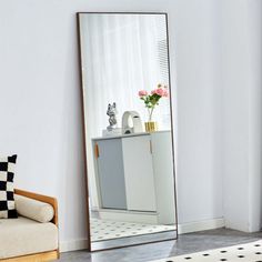 a mirror sitting on top of a white floor next to a couch and table with flowers