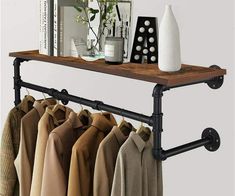 an iron pipe shelf with clothes hanging from it's sides and a vase on top