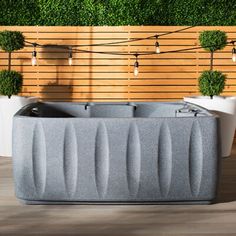 an outdoor hot tub in front of a wooden wall with potted plants and string lights