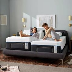 a man and woman laying on top of two beds in a room with hardwood floors