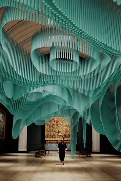 a woman walking through a large room with lots of blue pipes hanging from the ceiling