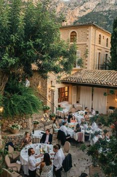 a group of people sitting at tables in front of a building with mountains in the background