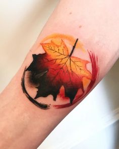 a leaf tattoo on the arm with red and orange leaves painted on it's side