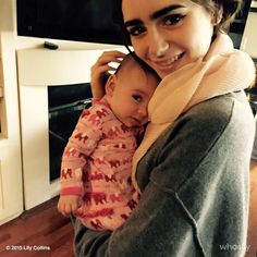 a woman holding a baby in her arms and smiling at the camera while standing next to an oven