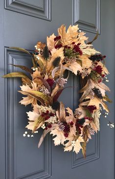 a wreath on the front door with flowers and leaves hanging from it's side