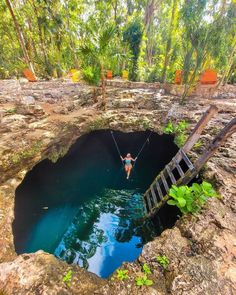 a person on a rope in the middle of a hole that is surrounded by trees