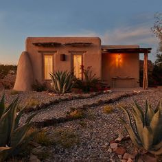 an adobe style home with cactus and succulents in the front yard at dusk