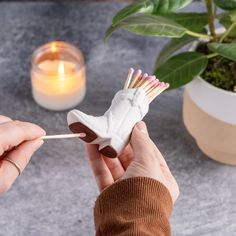 a person is holding a match stick with a shoe shaped matchestick in front of a potted plant