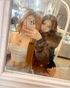 two women are taking a selfie in a window display with the reflection of them