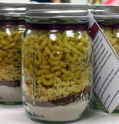 three jars filled with macaroni and cheese on top of a white tablecloth