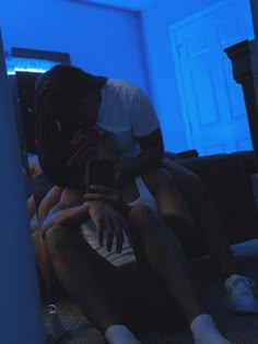 a man and woman sitting on the floor looking at their cell phones in a dark room