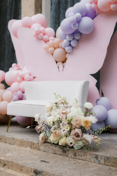 a white couch sitting on top of a stone floor next to flowers and balloons in the air