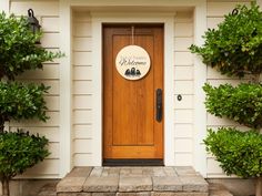 a welcome sign is on the front door of a house with potted trees and shrubbery