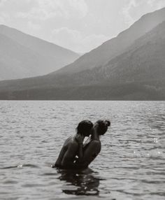 two people in the water kissing each other with mountains in the backgrouund