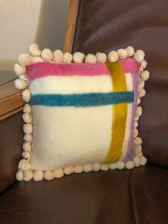 a pillow with pom - poms on it sitting on a leather couch next to a mirror