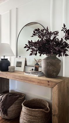 a wooden table topped with baskets next to a mirror and vase filled with purple flowers