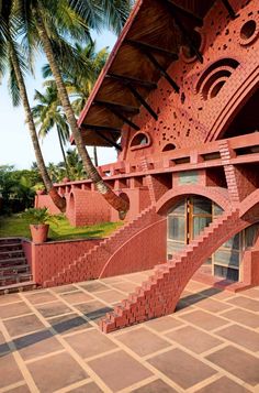 a red brick building with stairs leading up to the top floor and bottom level, surrounded by palm trees