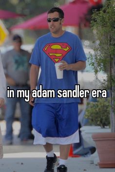 a man in a superman t - shirt is walking down the street with his drink