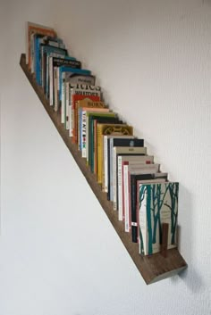 the books are lined up on the wall under the stair case, which is made out of wooden planks