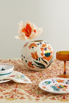 a table topped with plates and a vase filled with an orange flower sitting on top of a table