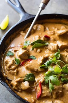 a skillet filled with curry and meat on top of a table next to a spoon