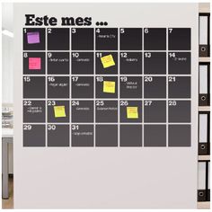 a wall calendar with sticky notes attached to it in an office setting that is white and black