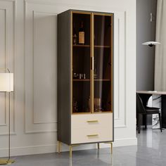 a tall cabinet with glass doors and gold trimmings in a living room next to a lamp