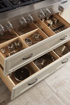 an open drawer with pots and pans in it on the floor next to a stove