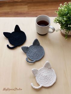 three crocheted coasters sitting on top of a table next to a cup of coffee