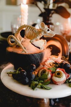 a table topped with a bowl filled with fruit and a skeleton figurine sitting on top of it