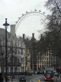 a red double decker bus driving down a street next to tall buildings and a ferris wheel