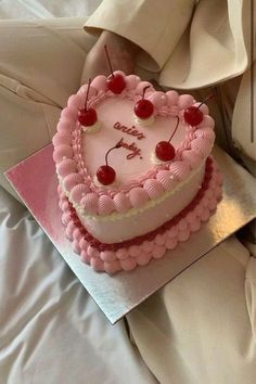 a heart - shaped cake with cherries on top is sitting on a bed, ready to be eaten