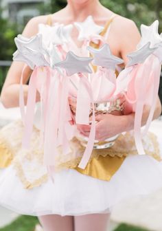 a woman in a tutu holding a bowl with silver stars on it and pink ribbons