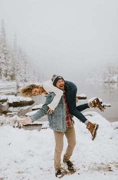 a man carrying a woman on his back in the snow near a body of water